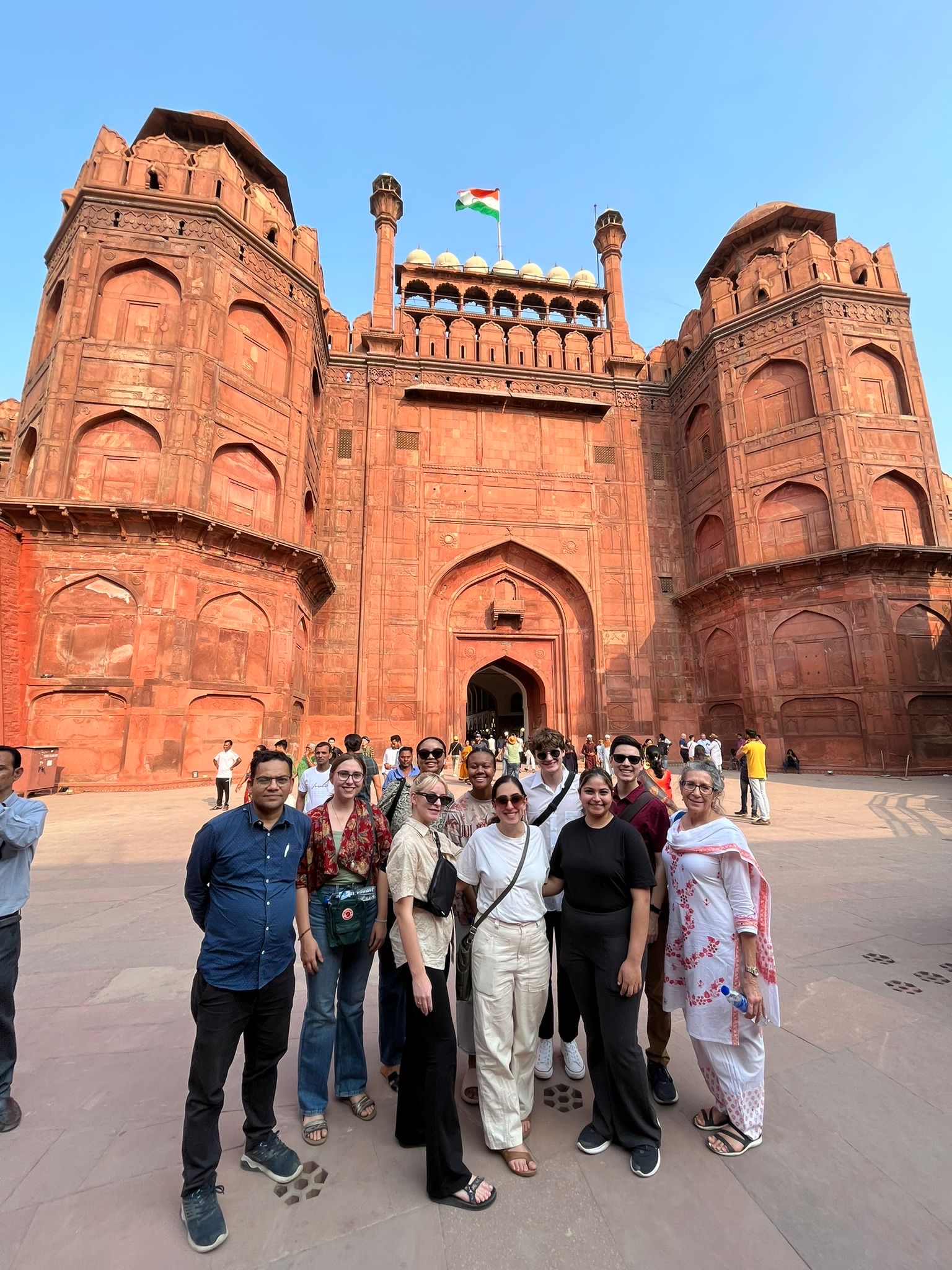 Group of people standing in front of large red-brown building with Indian flag