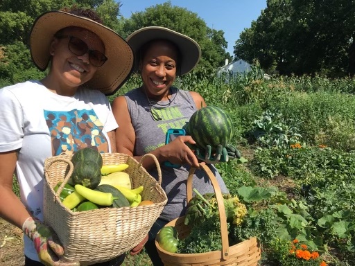 two women standing in a garden holding baskets with vegetables