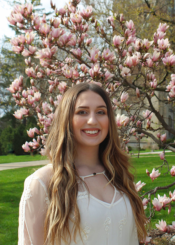 Emily McHarg stands in front of Beaumont Tower with cherry blossoms in the foreground