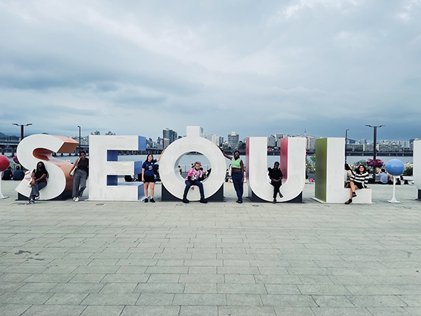 People sitting inside letters spelling out name of city Seoul