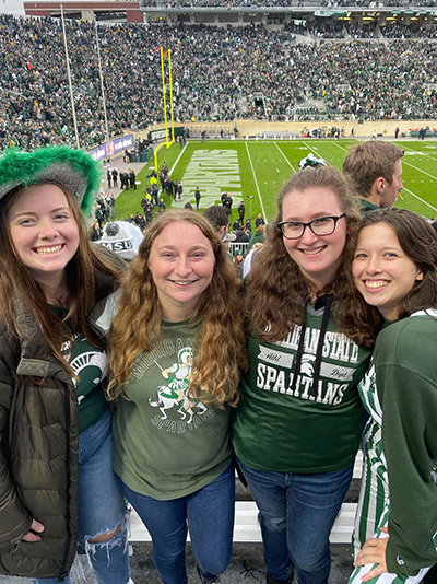 Four women standing arm in arm at a Spartan football game