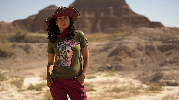 Woman standing in a desert wearing a hat and Frida Kahlo shirt