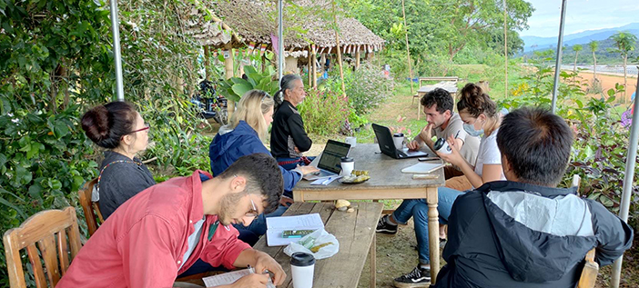 students and researchers gathered at a table beside the river under a shelter