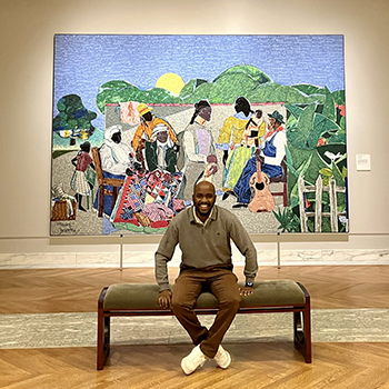Bevertone Anyonga sits on a bench in front of a large art piece at the Detroit Institute of Art