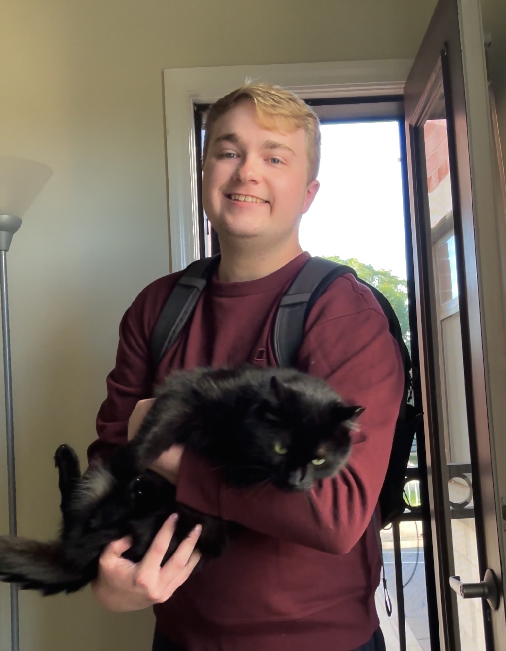 Noah Scudder stands in a doorway holding a cat